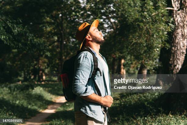 portrait  side view of a hispanic adult man with backpack breaths fresh air on the forest. - fresh air breathing stockfoto's en -beelden