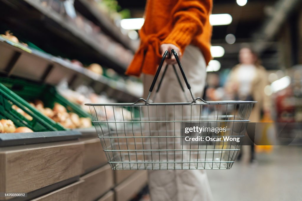 Cropper shot of young woman carrying a shopping basket while shopping in supermarket