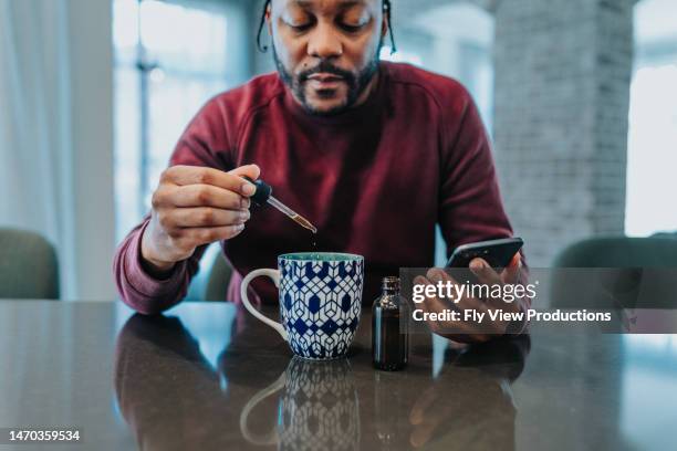 man adding cbd oil to his herbal tea - cbd oil stock pictures, royalty-free photos & images