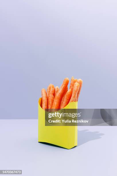 baby carrots in a yellow paper box on the purple background - vegan food - raw food diet stock pictures, royalty-free photos & images