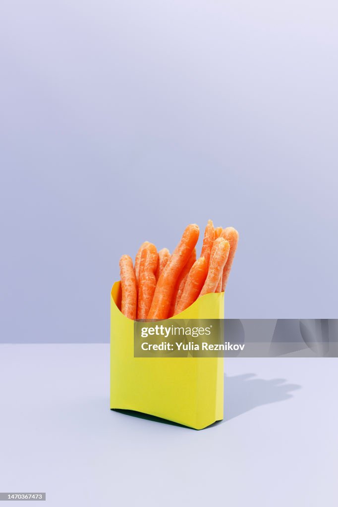 Baby carrots in a yellow paper box on the purple background - vegan food