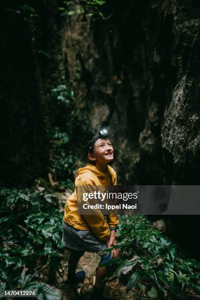 curious young girl exploring cave with headlamp - レインコート ストックフォトと画像