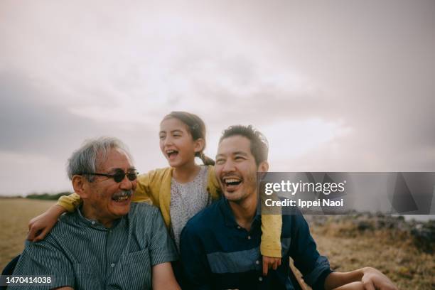 young girl having fun with her grandfather and father by sea at sunset - familia multigeneracional fotografías e imágenes de stock