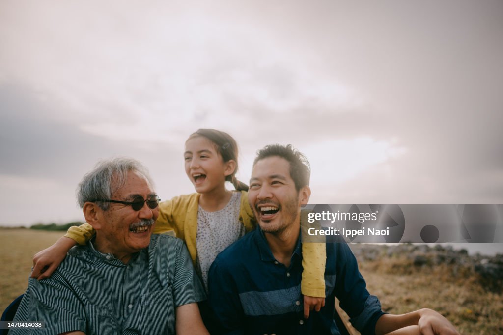Young girl having fun with her grandfather and father by sea at sunset