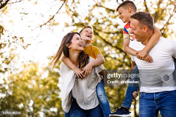 genitori allegri e i loro figli che si divertono mentre fanno il piggybacking in primavera al parco. - riserva naturale foto e immagini stock