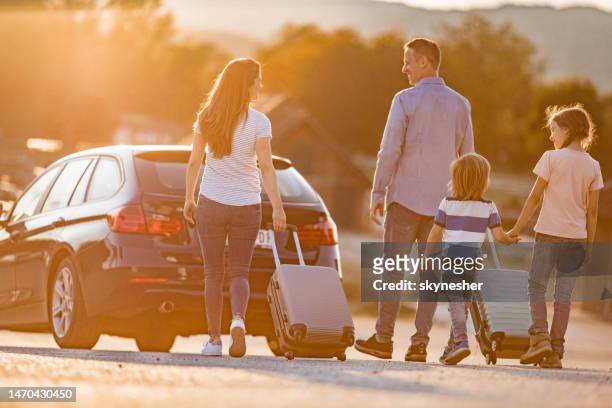 back view of happy family talking while pulling their suitcases on the street. - car sunset stock pictures, royalty-free photos & images