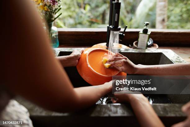 mother and daughter cleaning dishes under faucet - under sink foto e immagini stock