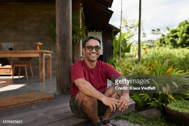 mature man sitting on steps at resort - rode korte broek stockfoto's en -beelden