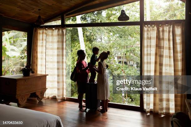 family standing near window in living room at villa - indonesia family stock pictures, royalty-free photos & images