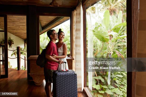 happy couple standing near window at villa - suitcase couple stockfoto's en -beelden