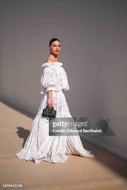 Sophia Roe wears a white cut-out lace pattern shoulder-off / bat short sleeves / long dress from Dior, a black shiny leather Lady handbag from Dior ,...