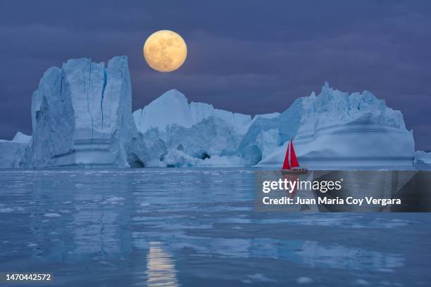 red sailboat sailing among floating icebergs in front of the full moon rising at arctic ocean in greenland, ilulissat icefjord, ilulissat, disko bay, unesco world heritage site - moon landscape stock pictures, royalty-free photos & images