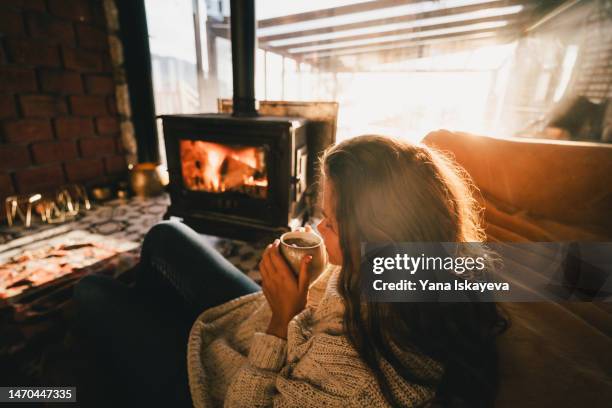 woman relaxing in front of the fireplace, embracing a mug with a hot drink - hot indoors stock pictures, royalty-free photos & images