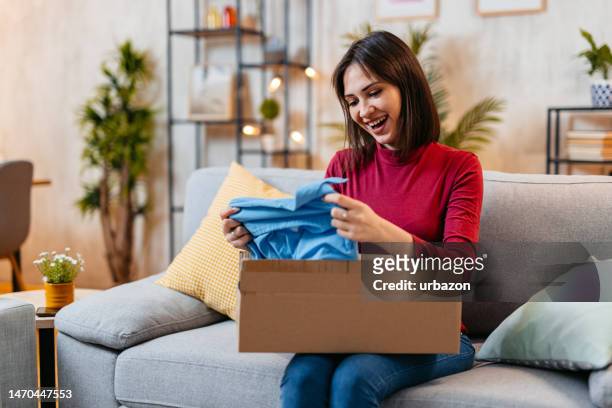 young woman unboxing a package with a new shirt she ordered online - online shopping opening package stock pictures, royalty-free photos & images