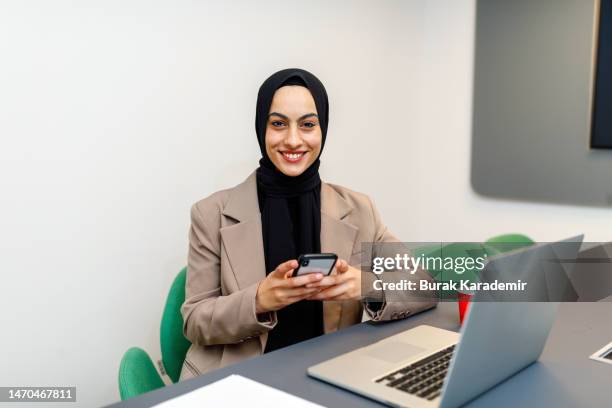 smiling young muslim woman using mobile phone and laptop - burka stock pictures, royalty-free photos & images
