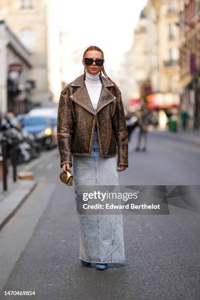 Guest wears black butterfly sunglasses, a white turtleneck t-shirt, a dark brown faded leather oversized zipper jacket, a pale blue denim long skirt,...