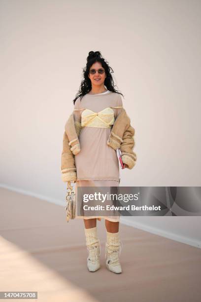 Guest wears black sunglasses, a white t-shirt, a beige double long knees t-shirt dress, a beige suede with embroidered sheep pattern aviator coat, a...