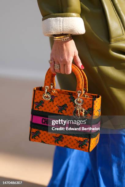 Guest wears a gold Love bracelet from Cartier, gold bracelets, a khaki shiny leather zipper oversized long coat with white sheep collar, royal blue...