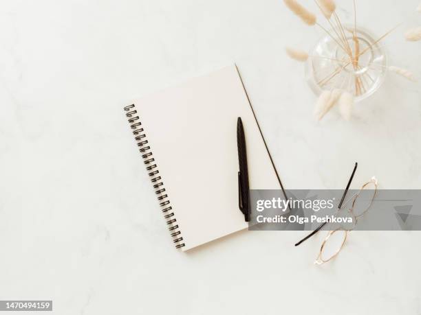 flat lay blank paper sheet in notebook, dry plants in vase, glasses and black pen on white background - office work flat lay stock pictures, royalty-free photos & images