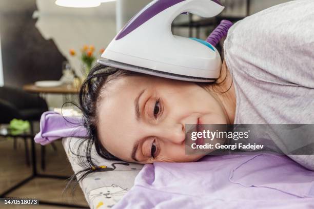 tired middle age woman lay down on an ironing board with an iron. - huisvrouw stockfoto's en -beelden