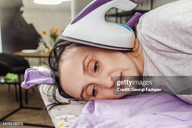 tired middle age woman lay down on an ironing board with an iron. - stereotypical housewife stock pictures, royalty-free photos & images