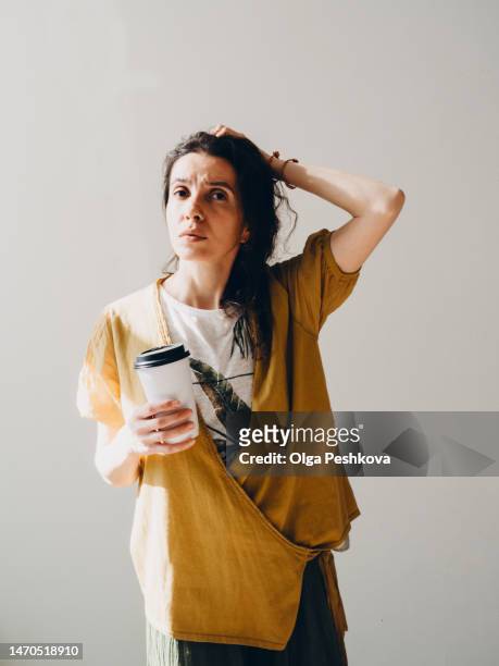 young woman holds white coffee cup, thought and looks to the right and raised her left hand to her hair - zeitumstellung stock-fotos und bilder