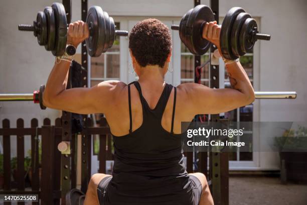 strong woman weightlifting with dumbbells in backyard - schulterpresse stock-fotos und bilder