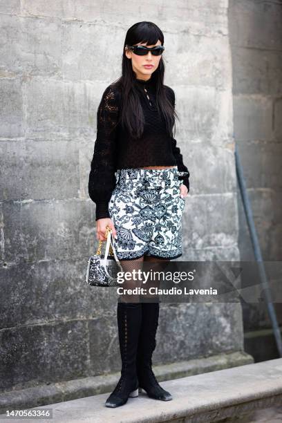 Livia Nunes Marques wears a black top, black and white printed shorts, matching Dior bag and black boots, outside Dior, during Paris Fashion Week -...