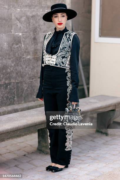 Ginevra Mavilla wears a black shirt, black and white decorated vest, black decorated trousers, Dior bag and hat, outside Dior, during Paris Fashion...