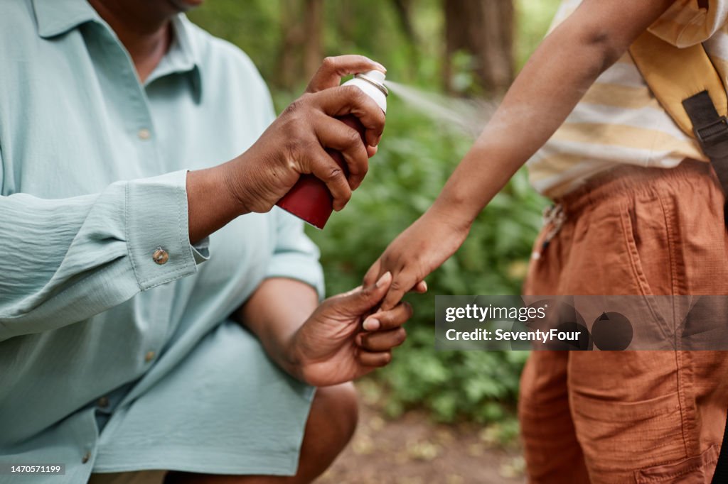 Closeup of caring black mother using baby safe bug repellent for daughter