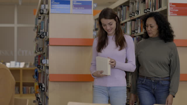 Young Adult Caucasian And Mid Adult Hispanic Female Joining A Senior Male In A Library