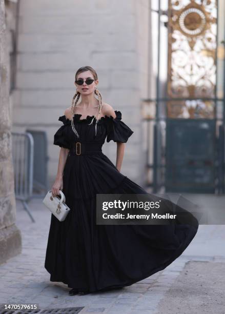 Xenia Adonts seen wearing a black shoulder free dress with a big black belt, black shades and a white bag before the Dior show on February 28, 2023...