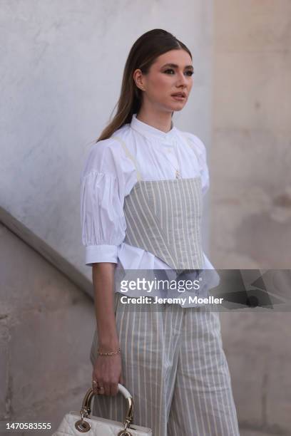 Zita d'Hauteville seen wearing a white blouse, a beige and white striped corsage and matching wide leg pants and a white bag before the Dior show on...
