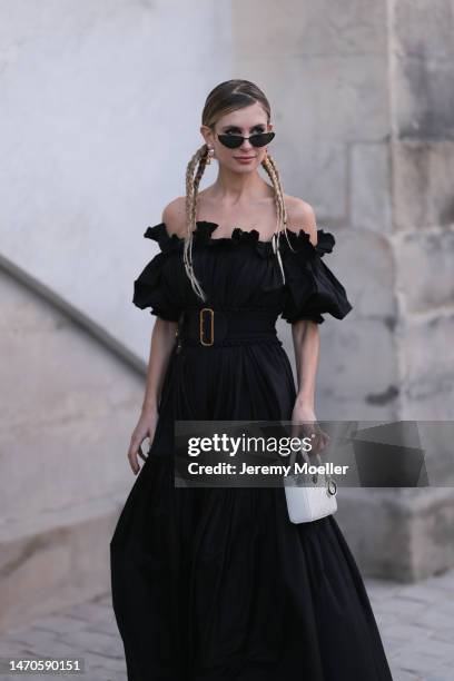 Xenia Adonts seen wearing a black shoulder free dress with a big black belt, black shades and a white bag before the Dior show on February 28, 2023...