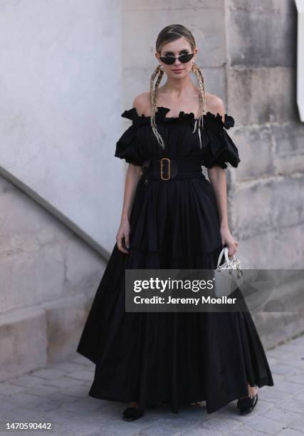 Xenia Adonts seen wearing a black shoulder free dress with a big black belt, black shades and a white bag before the Dior show on February 28, 2023...