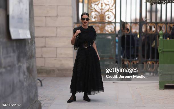 Camila Coelho seen wearing black shades, a black tulle dress, a black belt, black tights, a black Dior leather saddle bag and black heels before the...