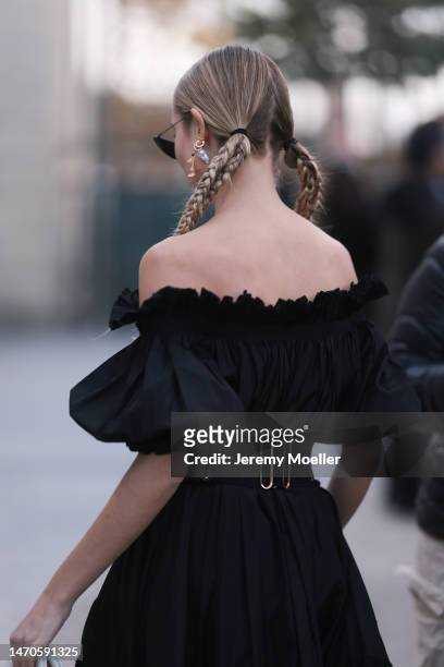 Xenia Adonts seen wearing a black shoulder free dress with a big black belt, black shades and a white bag before the Dior show on February 28, 2023...