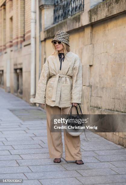 Joicy Muniz wears black bag with heart shape bag, bucket hat, belted jacket, brown pants, net shoes, sunglasses during Paris Fashion Week -...