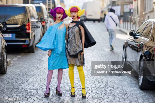 Twins Ami Amiaya wears blue dress, net tights and Aya Amiaya wears black dress, yellow tights, ear warmers outside Undercover during Paris Fashion...