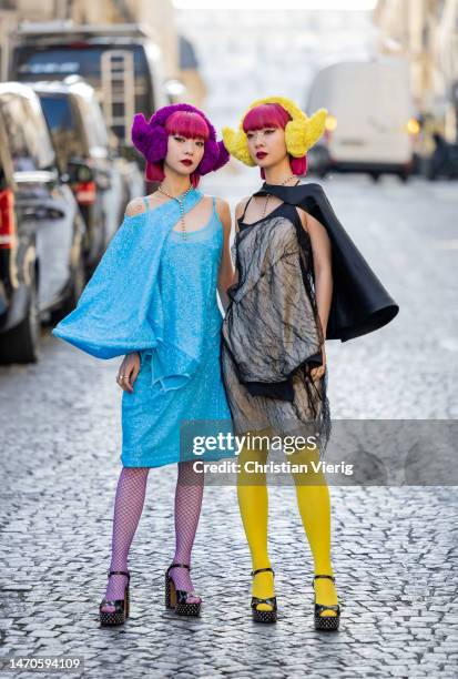 Twins Ami Amiaya wears blue dress, net tights and Aya Amiaya wears black dress, yellow tights, ear warmers outside Undercover during Paris Fashion...