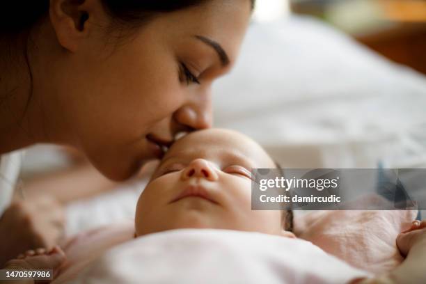 mother kissing her sleeping newborn baby - kissing baby stock pictures, royalty-free photos & images