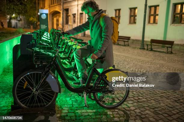 movilidad sostenible. hombre alquila bicicleta de ciudad por la noche. bss - economía colaborativa fotografías e imágenes de stock