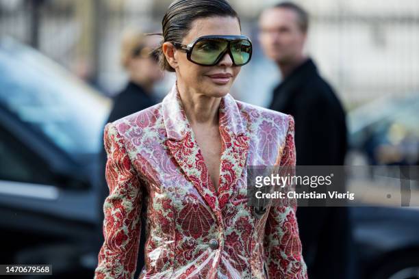 Guest wears sunglasses, varnished jacket with floral print in red, shorts, bag, boots outside Paco Rabanne during Paris Fashion Week - Womenswear...