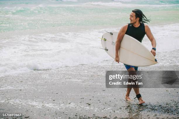 asian chinese male surfer walking on beach back from sea after riding wave in pacific ocean - adrenaline park stock pictures, royalty-free photos & images