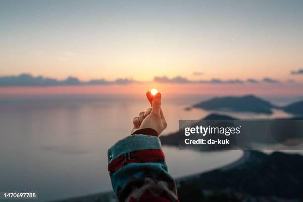 reise in ihrem herzen. frau macht herz aus fingern sonne bei sonnenuntergang - hands sun stock-fotos und bilder