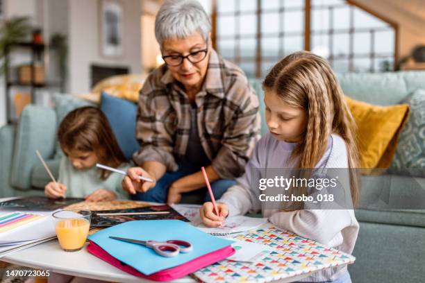 grandmother and two little girls drawing with wooden crayons at home - babysit stockfoto's en -beelden