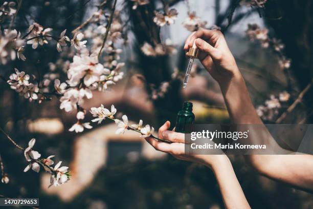 hand with pipette at spring flowers on background. - perfume stockfoto's en -beelden