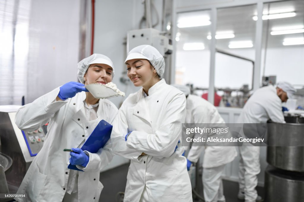 Two Female Food Processing Plant Workers Smelling Cottage Cheese Before Putting It In Filling Making Machine