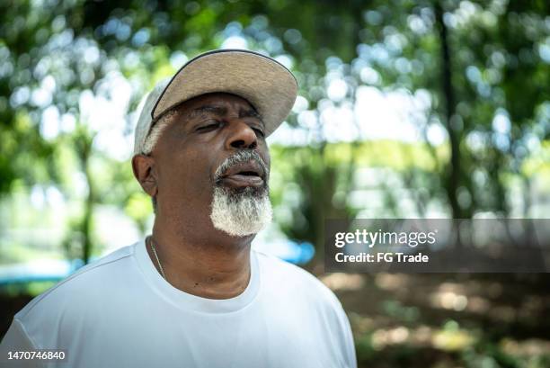 senior man doing breathing exercise in the park - exhale stock pictures, royalty-free photos & images