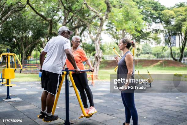 senior couple doing exercises with a personal trainer in the park - diversion stock pictures, royalty-free photos & images